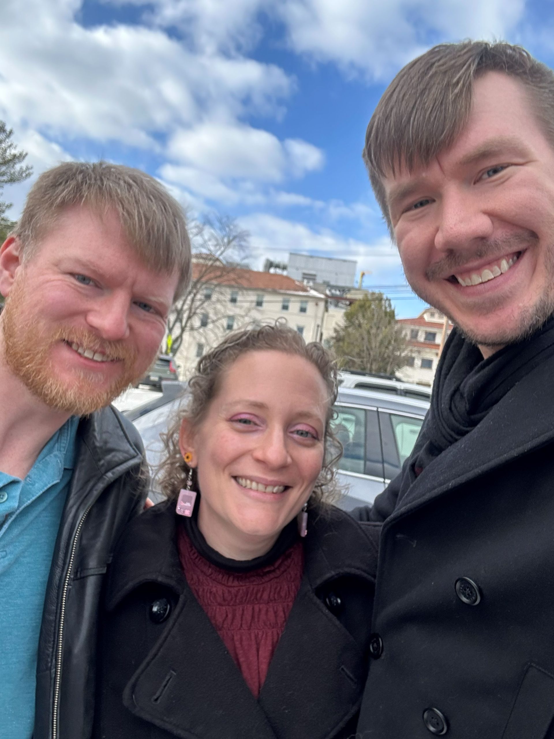 Photo of three people smiling. Surrogate is in the middle and Intended Dads are on either side of her.