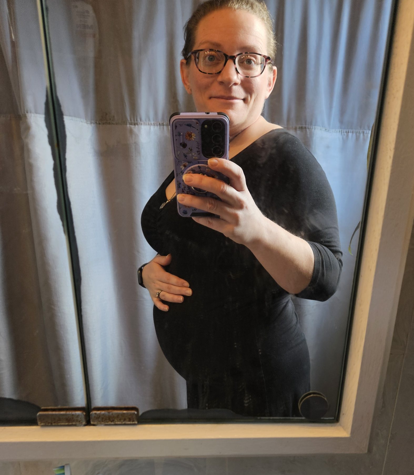 Surrogate mirror picture smiling and holding her pregnancy baby bump