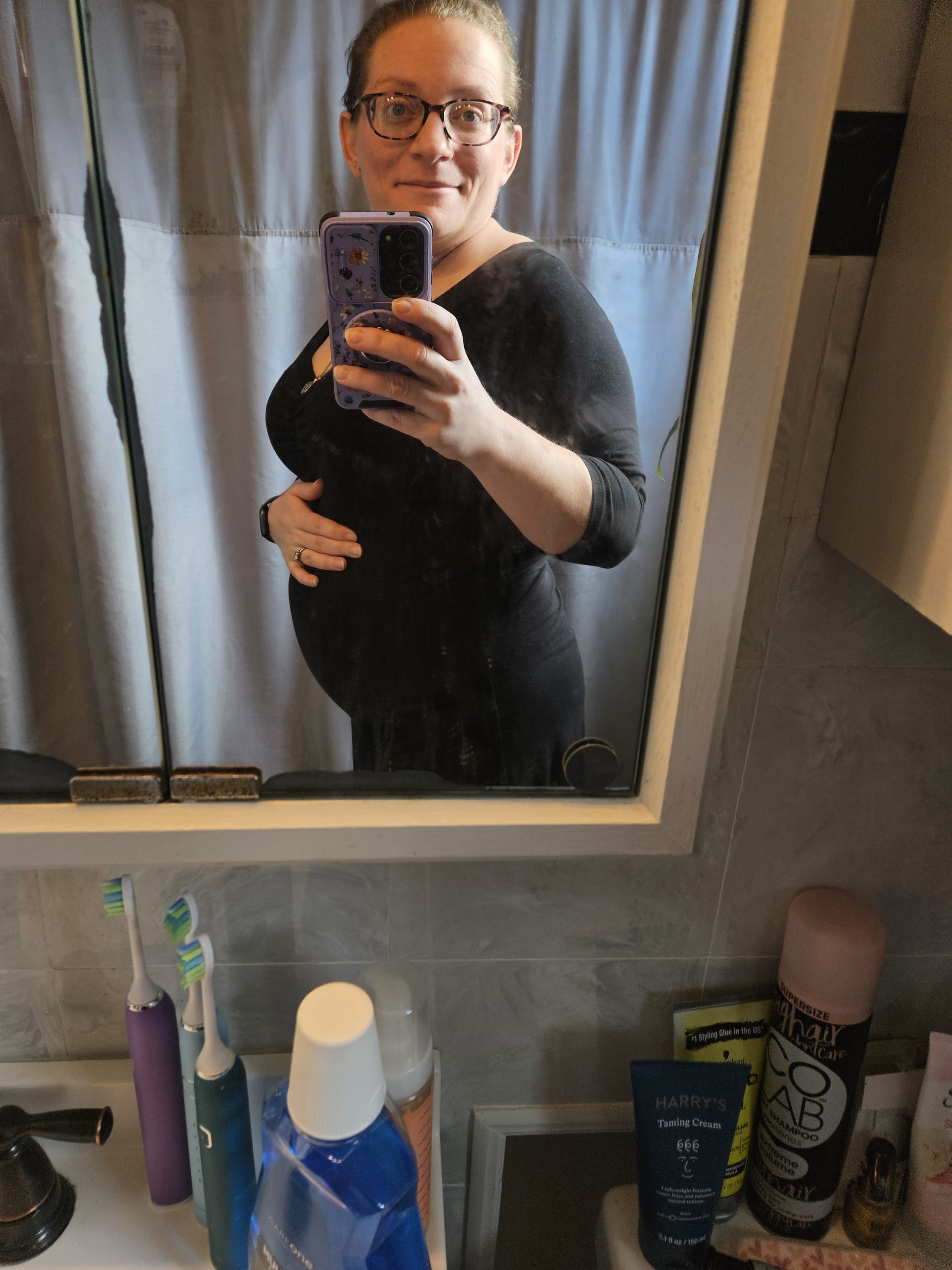 Surrogate mirror picture smiling and holding her pregnancy baby bump