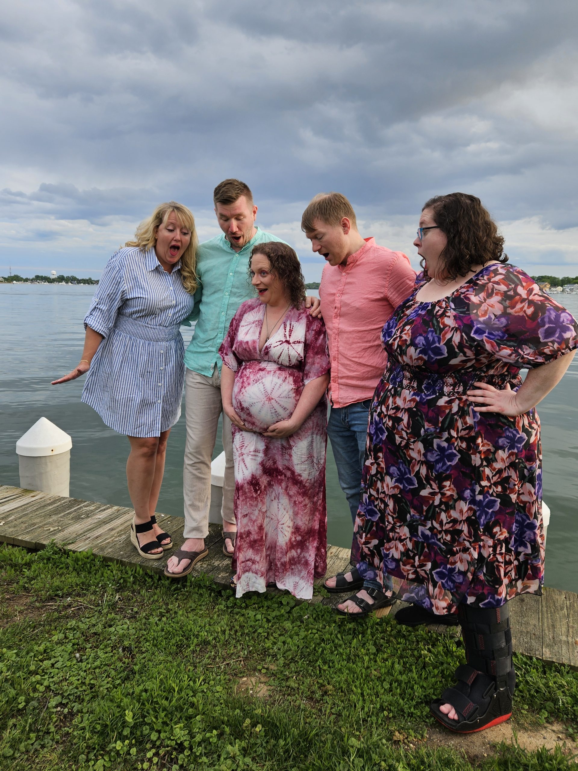 Four people standing in a row. Surrogate and Intended Parents in the middle and their supports to the side. They have happy and shocked faces looking at the baby bump.